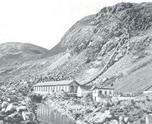 Petty Harbour Hydro-Electric Generating Station, c1900. Photo shows Newfoundland's first hydro-electric generating station, with the original line of the penstock half-way up the ridge.; From: Moses Harvey "Newfoundland at the Beginning of the 20th Century: a treatise of history and development." (New York: South Pub. Co., 1902) 176.