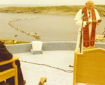 Pope John Paul II at the Blessing of the Fleet and Homily Site, Flatrock, with boats in the harbour in the background, on 1984/09/12.; Courtesy Archives of the Roman Catholic Archdiocese, St. John's, NL.