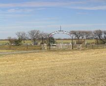 View northeast showing gate, fence, memorial cairn and wooden cross, 2005.; Government of Saskatchewan, Marvin Thomas, 2005.