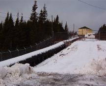 Exterior view of the wooden flume constructed by Bernard J. Miller (1877-1949).  This flume was the first of its kind built in Newfoundland. The substation can be seen in the upper right corner. Photo taken January 2006.; HFNL/ Lara Maynard 2006.