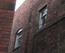 This image provides a view of the side of the building, including a segmented arched opening alongside a rectangular opening with sandstone sills and lintel, possibly revealing an idea of what the building may have looked like in its original state, 2005.; City of Saint John