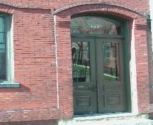 This photograph shows the wooden door and transom window under the arched entranceway, 2004; City of Saint John