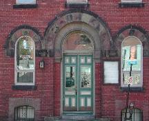 This photograph shows the wooden door, the roman arch transom window and Roman arch windows on each side of the elaborate entrance, 2004; City of Saint John