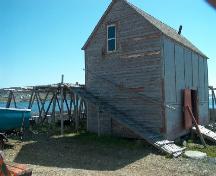 Exterior view of fish flake and of gable end and entrance side of the net store of Samuel Abbott Fishing Room, Newman's Point, Bonavista, NL, circa 2006; Bill Abbott/HFNL 2006