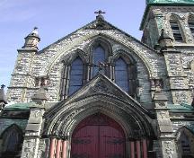 This photograph shows the ornate detailing, the large gothic window, pinnacles, supporting corinthian columns, gothic arched door and entranceway, crosses, and flag bearing lamb insignia, 2004; City of Saint John
