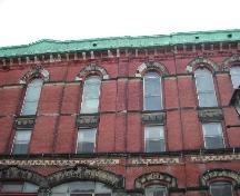 This photograph shows the metal cornice with brackets and the Roman arch and square windows on the top two floors, 2004; City of Saint John