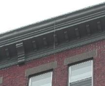 This image provides a view of the cornice supported by regularly placed wooden brackets, 2005.; City of Saint John