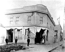 Exterior view of the Syndicate Block, c. 1907: The Express newspaper office to the left; J.A. McMillan Grocery at corner; North Vancouver Museum and Archives, #6594
