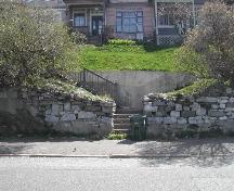 This photograph shows the access way to the complex with natural bedrock foundation along with placed stones for the wall and wooden stairways, 2005; City of Saint John