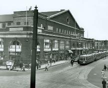 The south (Sainte-Catherine Street) façade of the Montreal Forum in April of 1947, showing the original appearance of the structure with its commercial premises along the south and west (left side of the photograph) elevations.; Library and Archives Canada, PA129603, from the National Film Board, Phototèque Collection/ Bibliothèque et Archives Canada, PA129603, Office national du film du Canada, Collection Phototèque, 1947.