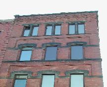 Photograph showing the upper stories and illustrating the windows, recessed brickwork, sandstone ledge, cornice, corbel bands, and sandstone courses; City of Saint John 2004
