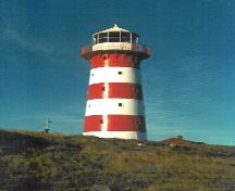 View of the Cape Pine Lighthouse, showing the smooth, painted finish of the exterior walls with its distinguishing colour scheme of alternating white and red, 1990.; Agence Parcs Canada / Parks Canada Agency, 1990.