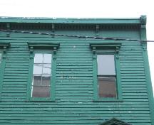 Cette photographie montre deux fenêtres des étages supérieurs, ainsi que la corniche de la ligne de toit munie de dentelets et de consoles, 2005; City of Saint John