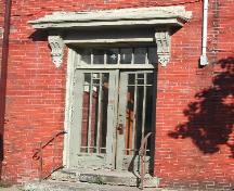 This photograph shows the wooden door with glass panels, transom window, and heavy decorative entablature, 2004; City of Saint John