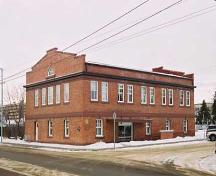 This photograph illustrates the secondary west and south brick clad two storey facades of the North Telephone Exchange with a prominent end pediment. Also illustrated is the large rear access door with lifting beam for installing and removing equipment.; City of Edmonton, 2004