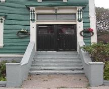 This image provides a view of the entry with an entablature supported by brackets, a two-paned transom window and paired wood doors with glass panels, 2005; City of Saint John