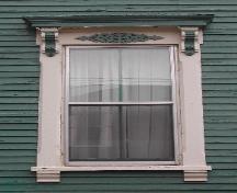 This image provides a view of a vertical sliding wood window below an entablature supported by ornate brackets, 2005; City of Saint John