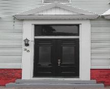 This image provides a view of the entry consisting of a pediment above a transom window and paired wood doors with glass panels, 2005; City of Saint John