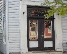 This photograph shows the entrance to the building, and illustrates the segmented arch transom window over the wooden doors with glass panels, 2005; City of Saint John