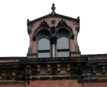 This image provides a view of the pedimented dormer with a finial, Roman arch windows and the bracketed cornice, 2005; City of Saint John