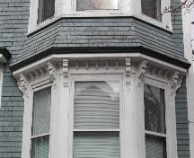 This photograph shows the flared bracketed cornice between the first and second floor of the bay window, 2005; City of Saint John