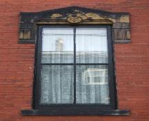 This image provides a view of a wooden window with a sandstone pediment lintel, 2005; City of Saint John