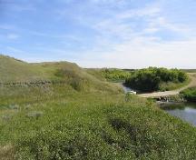 Archaeological remains were exposed in grassed-over road cut, left middle ground, 2004.; Government of Saskatchewan, Marvin Thomas, 2004.