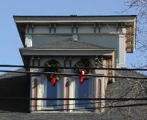 Cette image montre le belvédère et la lucarne centrale avec un toit en croupe et des fenêtres doubles à arc en plein cintre au-dessus d'une corniche en bois soutenue par une série de consoles doubles en volute, 2006; City of Saint John
