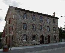 General view of the Old Stone Mill, showing its neo-classical, exterior detailing, including its bays trimmed with graceful, segmentally arched, stone voussoirs, 2004.; Parks Canada Agency / Agence Parcs Canada, 2004.