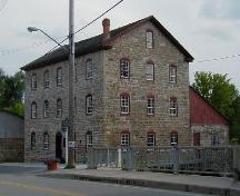Vue en angle du vieux moulin en pierre, qui montre sa composition constituée de façades à cinq baies et de façades latérales à trois baies, 2004.; Parks Canada Agency / Agence Parcs Canada, 2004.