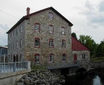 Side view of the Old Stone Mill, showing its masonry construction with exterior walls of uneven coursed local stone with heavy stone corner quoins, 2004.; Parks Canada Agency / Agence Parcs Canada, 2004.