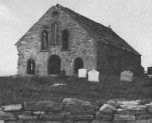 Historic photo view facing front of former Roman Catholic stone church with cemetery, looking west, Torbay, NL, circa 1900; Torbay Museum, 2006