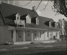 View of Governors' Cottage, showing its verandah with columns and the small, second-floor balcony, 1973.; Agence Parcs Canada / Parks Canada Agency, 1973.