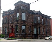 This image shows the Romanesque Revival entryway, classical ornamentation and pediment forms, medieval ornamentation of undercut sandstone, Queen Anne Revival massing, large window openings and heavy quarry-cut ashlar masonry laid in Scotch bond; City of Saint John