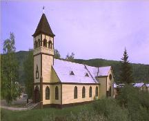 General view of St. Paul's Anglican Church, showing the rectangular massing under a steep gabled roof with truncated transepts, polygonal apse, and  tower with pyramidal, bell-cast roof.; Parks Canada Agency / Agence Parcs Canada.