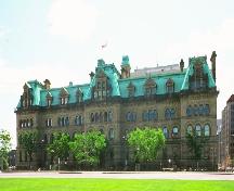 Vue générale de l'édifice Langevin, qui montre son style Second Empire attesté par son haut toit en mansarde ponctué de lucarnes à un et deux étages mettant  en relief la qualité tridimensionnelle de la silhouette.; Parks Canada Agency / Agence Parcs Canada.