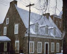 Vue en angle de la maison Hertel de La Fresnière au complexe historique de Trois-Rivières, qui montre le toit à deux pignons pourvu de lucarnes et les cheminées logées dans les murs pignons.; Parks Canada Agency / Agence Parcs Canada