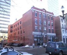 This image illustrates the front, west-facing, primary brick-clad facade of the Armstrong Block showing the commercial uses at ground level with three floors of residential uses above.; City of Edmonton, 2004