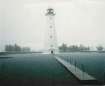 Vue générale du phare, qui montre la forme et le volume du bâtiment, sa silhouette élancée et la plate-forme évasée surmontée d’une lanterne de fer, 1986.; Canadian Coast Guard / Garde côtière canadienne, 1986.