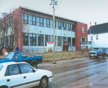 Vue de la façade principale de l'édifice du gouvernement du Canada, qui montre les fenêtres et les panneaux d’allège en bandeau qui rehaussent l’horizontalité des façades, 1996.; Parks Canada Agency / Agence Parcs Canada, 1996.