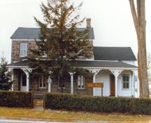 Façade of the Superintendent's Residence, showing the two-storey rectangular massing with a gently sloping pitched roof, chimney stack and pitched roof wood extension, 1977.; Parks Canada Agency / Agence Parcs Canada, 1977.
