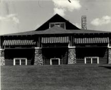 Vue générale du pavillon de golf (B7), qui montre la construction en rondins posés à  l’horizontale et les détails en pierre, 1984.; Agence Parcs Canada / Parks Canada Agency, 1984.