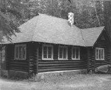 View of the Royal Canadian Air Force Cottage, showing the peeled log walls and shingled roof with chimney, 1984.; Agence Parcs Canada / Parks Canada Agency, 1984.