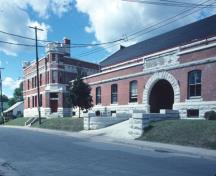 View of Peterborough Armoury, showing the large scale and massing which include the front and rear double-storied façades flanked by crenellated corner towers, 1980.; Agence Parcs Canada / Parks Canada Agency, 1980.