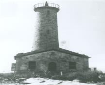 General view of the Lighthouse at Mohawk Island, showing the hammer-dressed finish on the stone walls of the tower and dwelling, giving a heavily rusticated appearance, before 1965.; Department of the Environment / Ministère de l'Environnement, before 1965 / avant 1965.