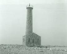 General view of the Lighthouse at Mohawk Island, showing the building’s tall profile, cylindrical form and the integration of the simple residence, ca. 1980.; Department of the Environment / Ministère de l'Environnement, ca./vers 1980.