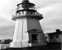 Vue du phare, qui montre son volume conique formé d’un court fût couronné d’une lourde balustrade en béton.; Garde côtière canadienne / Canadian Coast Guard