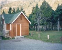 Corner view of Comfort Station 6, showing the cross-gable roof and the use of half-log slab siding for the walls, 1990.; Parks Canada Agency / Agence Parcs Canada, 1990.