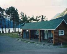 General view of Kitchen Shelter 2, showing the moderately pitched gabled roof with exposed rafters and log slab siding for the walls, 1990.; Parks Canada Agency / Agence Parcs Canada, 1990.