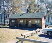General view of Kitchen Shelter 6, showing the moderately pitched gabled roof with exposed rafters and log slab siding for the walls, 1990.; Parks Canada Agency / Agence Parcs Canada, 1990.